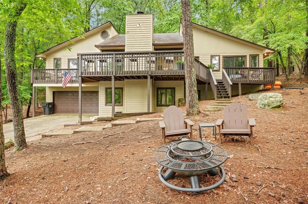 Back of house featuring an outdoor fire pit, a wooden deck, stairs, concrete driveway, and a chimney