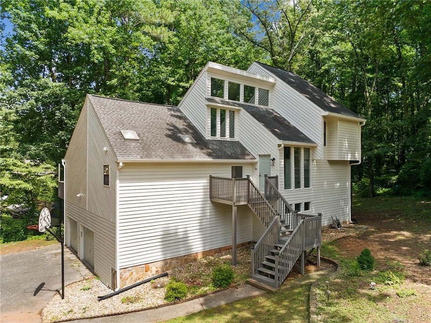 View of front of property featuring stairway, a shingled roof, asphalt driveway, a garage, and view of wooded area