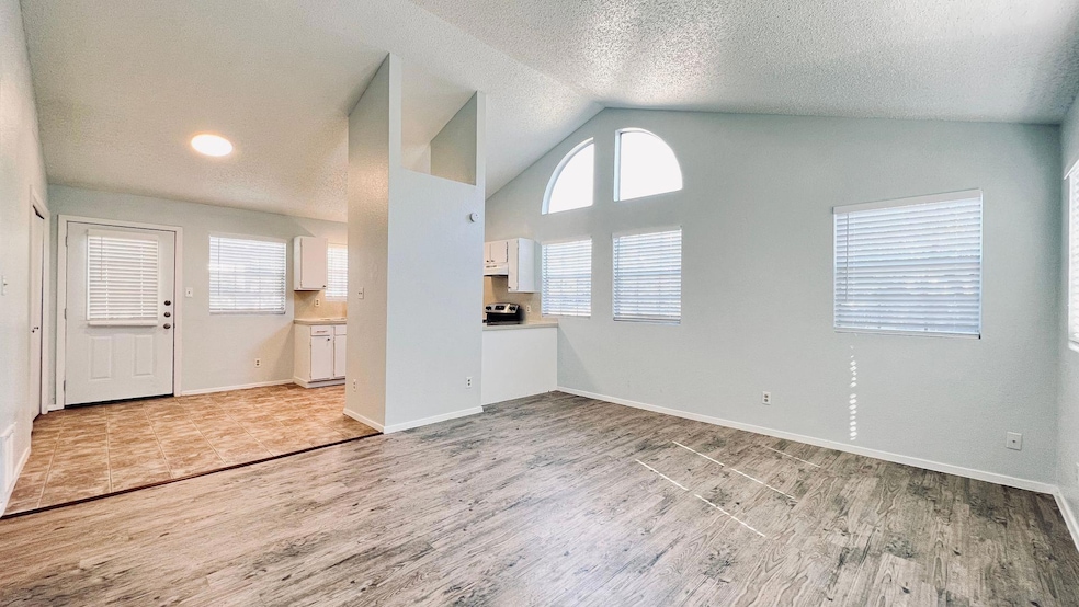 Unfurnished living room with light wood-style floors, a textured ceiling, and high vaulted ceiling