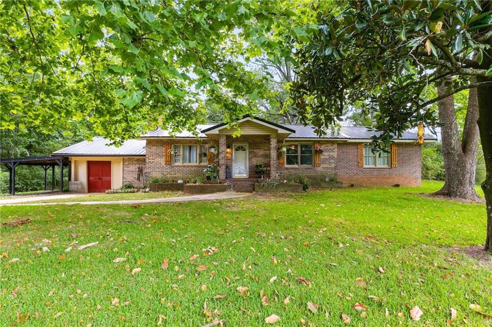 View of front facade with brick siding, a front yard, an attached carport, and a metal roof