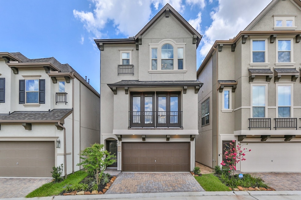 This is a modern, three-story townhouse with a two-car garage and a small, landscaped front yard. It features a neutral exterior with a balcony on the second floor, providing a sleek and stylish look.