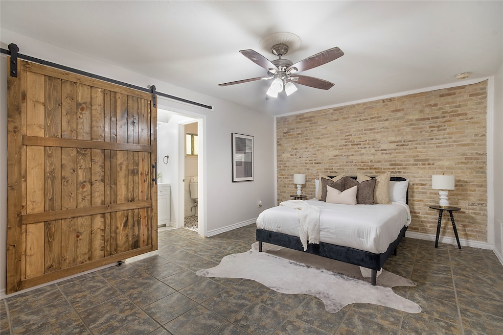 Bedroom with a ceiling fan, brick wall, a barn door, and connected bathroom