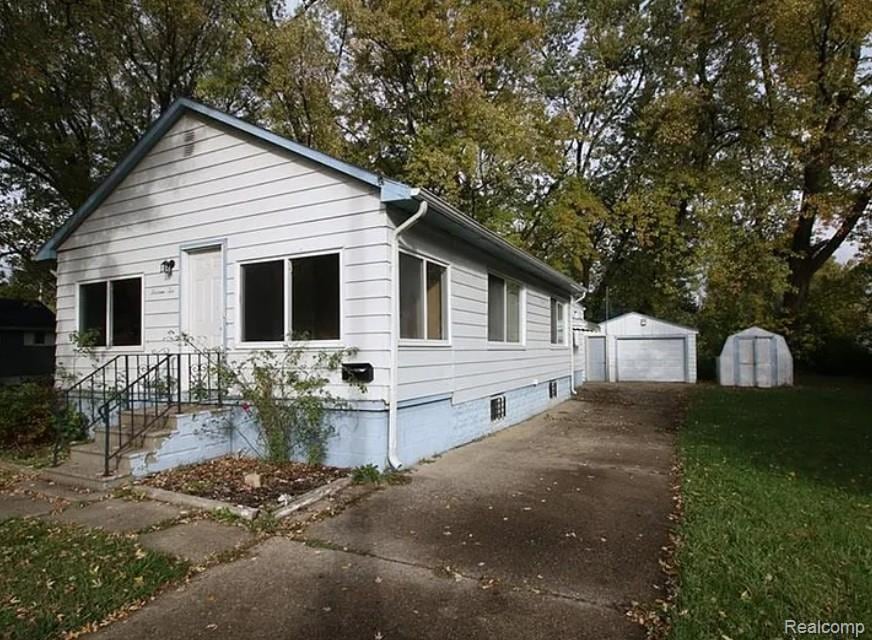View of property exterior with an outdoor structure, driveway, a garage, view of scattered trees, and a lawn