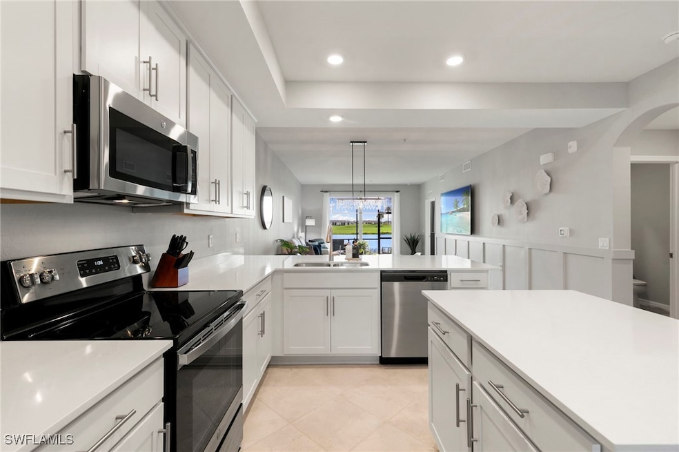 Kitchen with appliances with stainless steel finishes, white cabinetry, decorative light fixtures, recessed lighting, and arched walkways