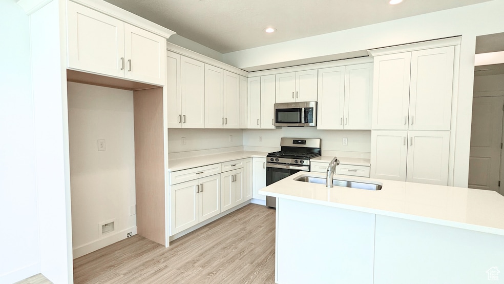 Kitchen with appliances with stainless steel finishes, white cabinetry, light wood-style flooring, light stone countertops, and recessed lighting (pictures are of a previous home built)