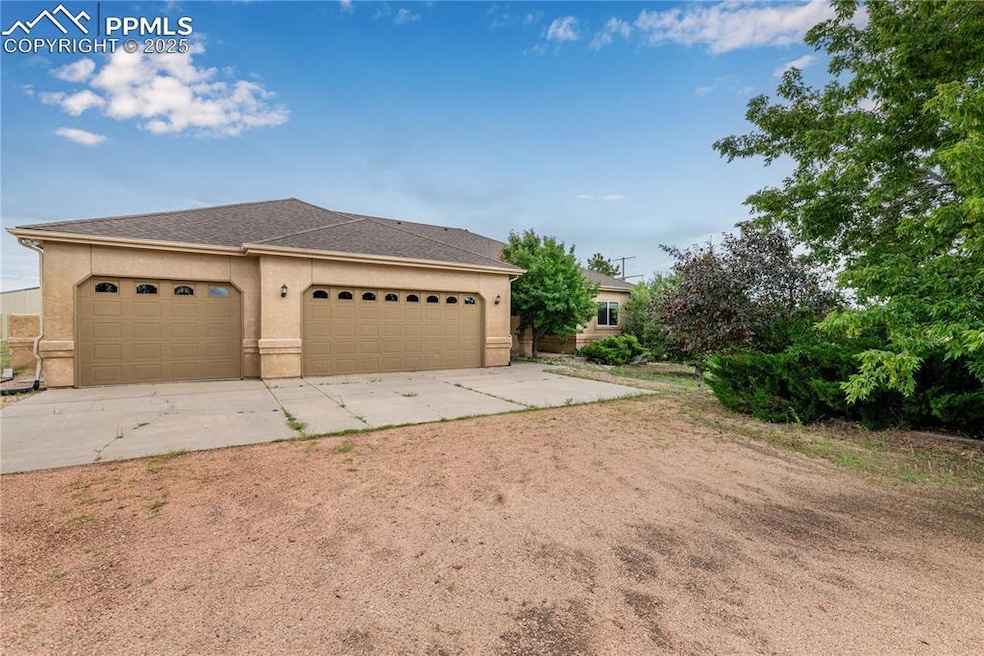 View of front facade with driveway, a shingled roof, a garage, stucco siding, and an outdoor structure