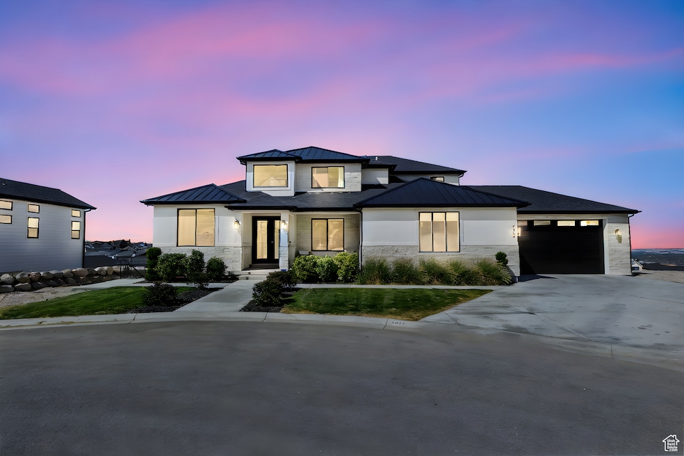 View of front of home featuring a standing seam roof, a metal roof, an attached garage, concrete driveway, and stone siding