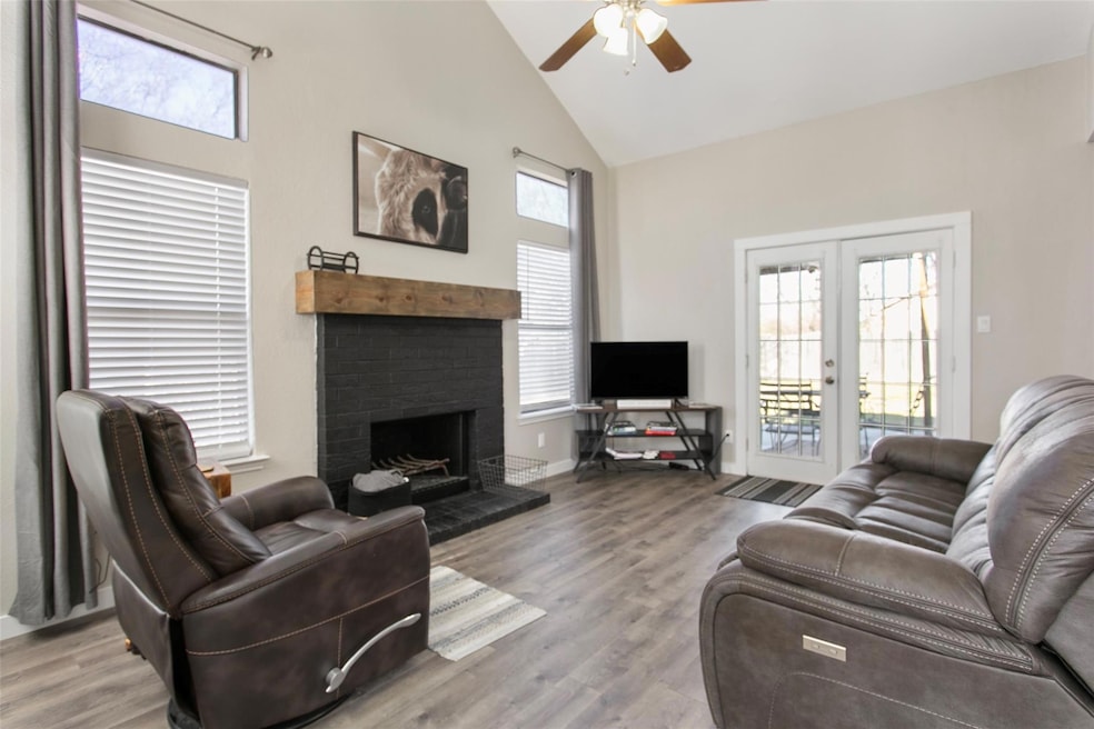 Living room featuring high vaulted ceiling, french doors, ceiling fan, a brick fireplace, and light hardwood / wood-style flooring