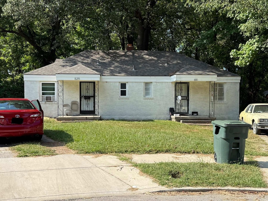 View of front of property with a shingled roof, brick siding, a front lawn, and view of wooded area