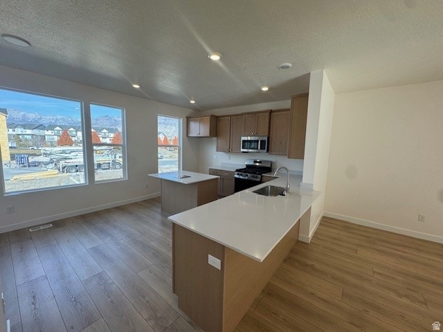 Kitchen with brown cabinets, a textured ceiling, range with gas stovetop, a peninsula, and light wood-style floors