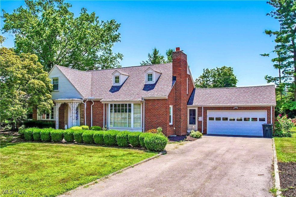 Cape cod-style house with a chimney, brick siding, an attached garage, a front yard, and driveway