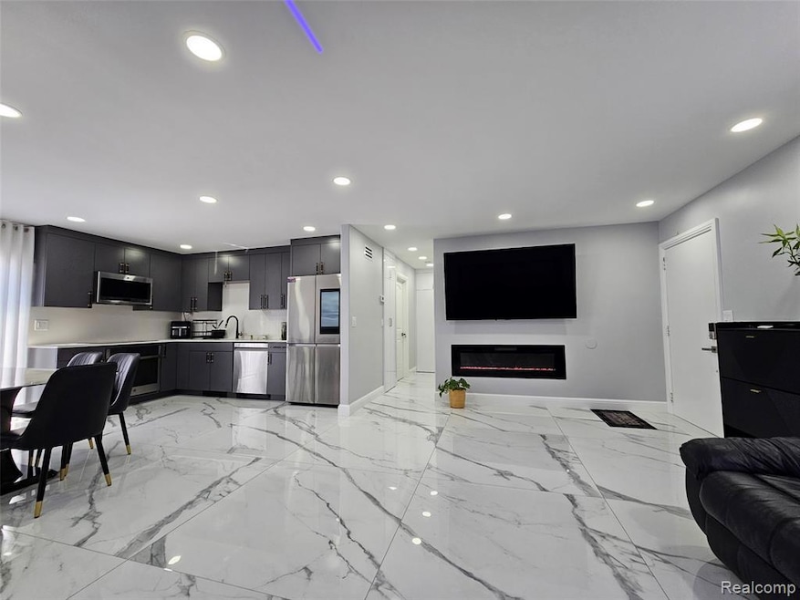 Living area featuring light marble finish floors, a glass covered fireplace, and recessed lighting
