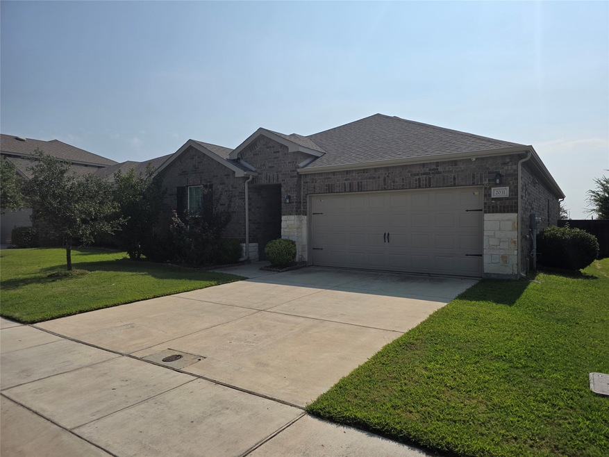 Ranch-style house with a front yard, brick siding, concrete driveway, roof with shingles, and stone siding