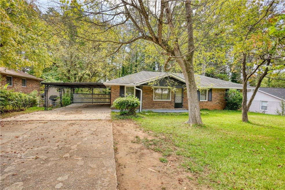 Single story home featuring driveway, a front yard, brick siding, and view of wooded area