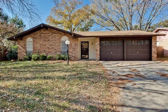 Single story home featuring brick siding, an attached garage, a front lawn, and driveway