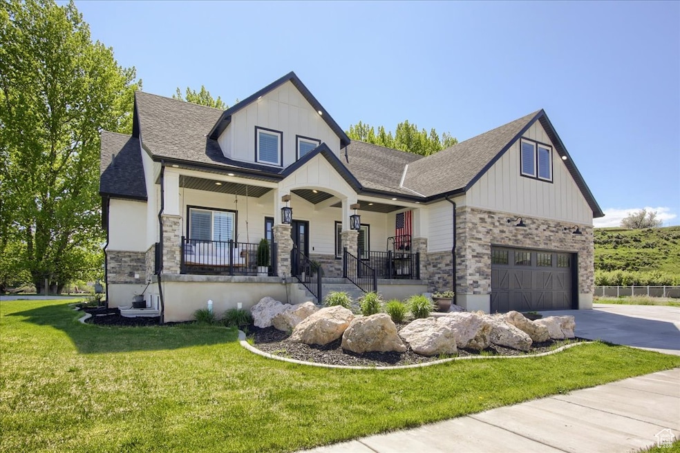 View of front facade with a porch, board and batten siding, a front yard, a shingled roof, and stone siding