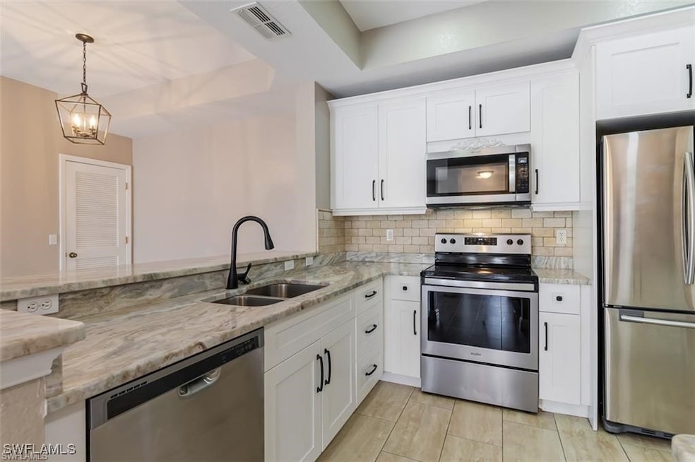 Kitchen featuring sink, stainless steel appliances, white cabinets, and hanging light fixtures