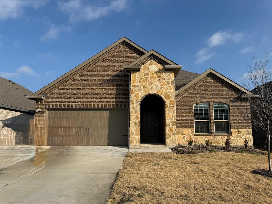 French country inspired facade featuring stone siding, brick siding, an attached garage, concrete driveway, and a front lawn