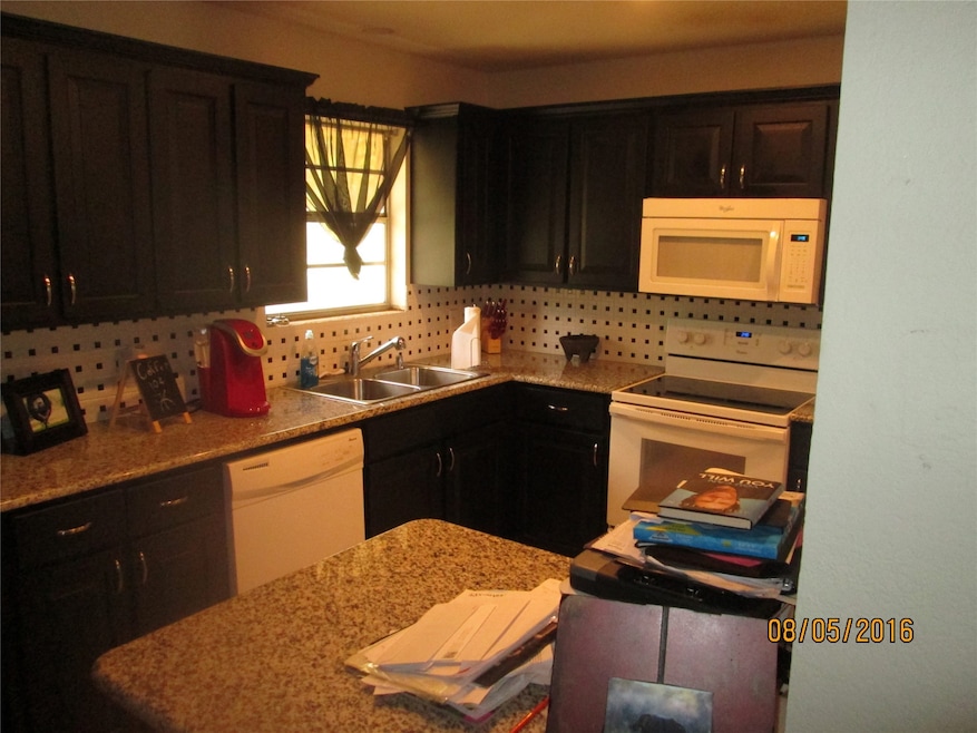 Kitchen featuring white appliances, backsplash, and light stone counters