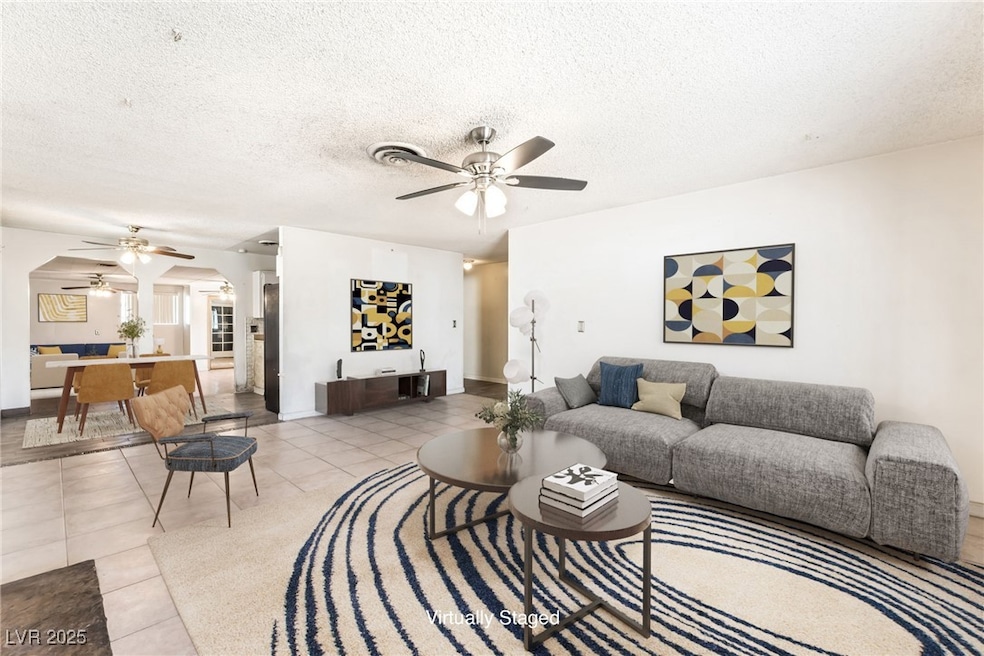 Living room featuring a ceiling fan, arched walkways, tile patterned floors, and a textured ceiling