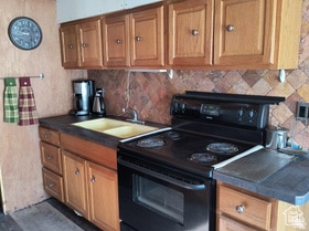Kitchen with black range with electric cooktop, dark countertops, brown cabinets, and tasteful backsplash