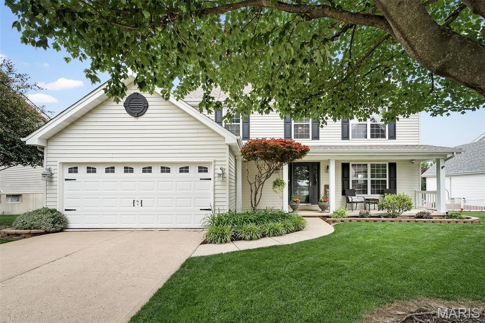 View of front facade with covered porch, driveway, a front yard, and a garage