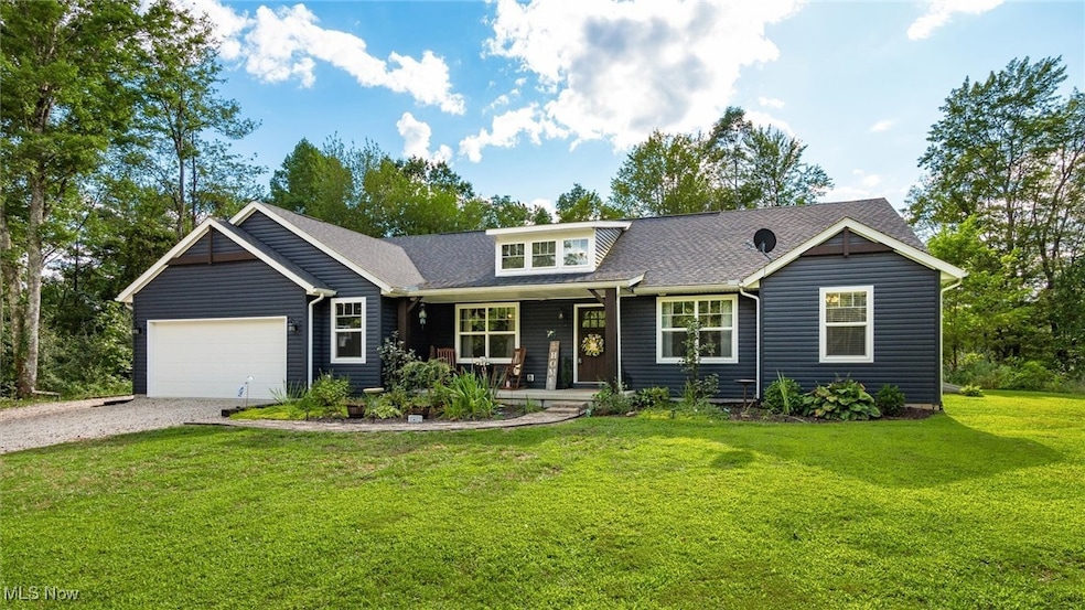 View of front of house with gravel driveway, covered porch, an attached garage, a front yard, and a shingled roof