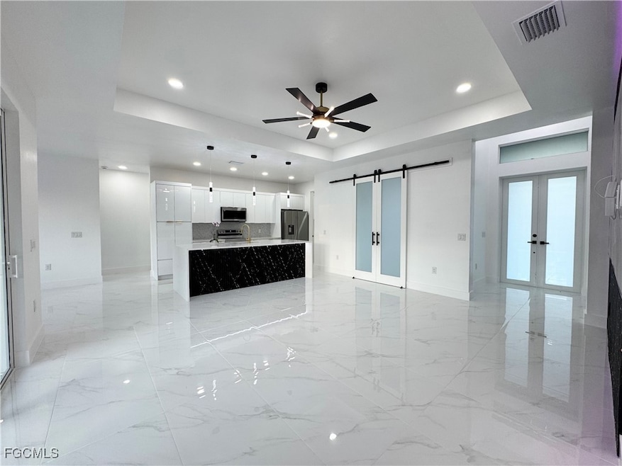 Unfurnished living room featuring a raised ceiling, a barn door, french doors, recessed lighting, and light marble finish flooring