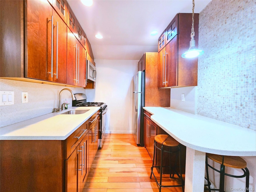 Kitchen featuring brown cabinetry, stainless steel appliances, tasteful backsplash, light wood-type flooring, and a kitchen breakfast bar