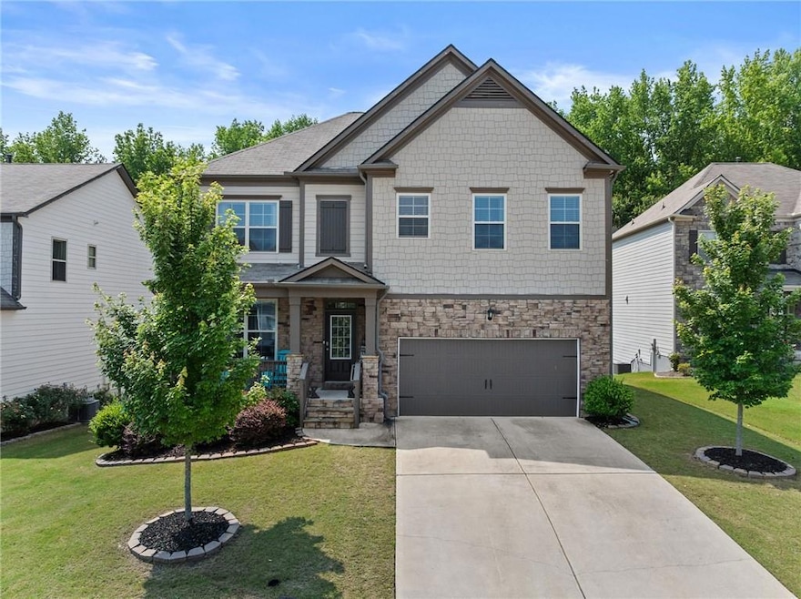 Craftsman-style home featuring an attached garage, driveway, stone siding, and a front lawn
