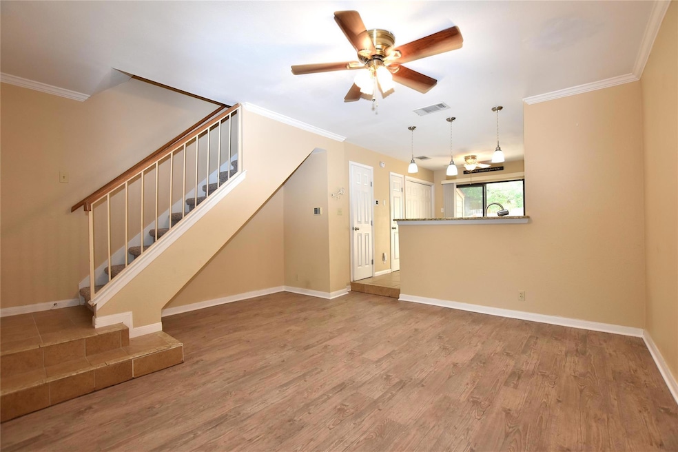 Unfurnished living room with wood finished floors, a ceiling fan, stairs, ornamental molding, and baseboards