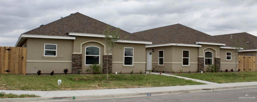 View of front of home with stucco siding, roof with shingles, a gate, and stone siding