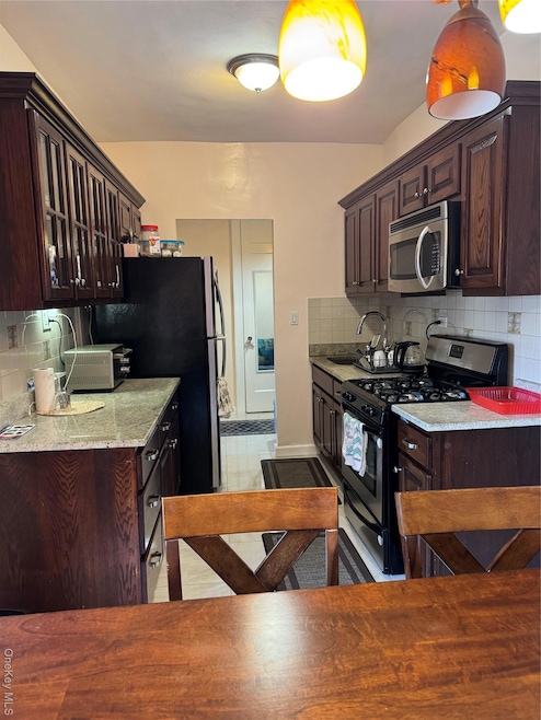 Kitchen with backsplash, dark brown cabinets, black stove, and stainless steel microwave