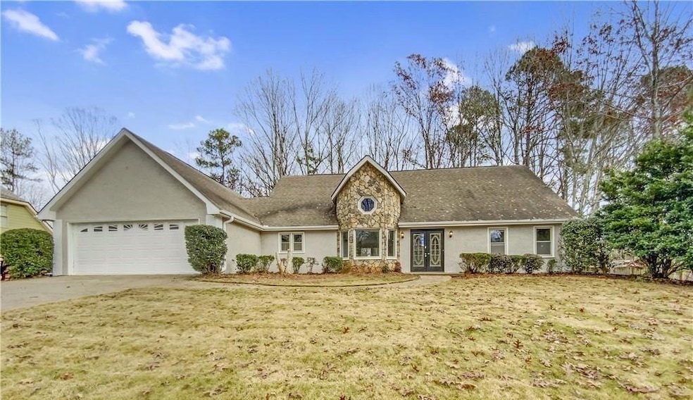 Ranch-style home with stone siding, stucco siding, an attached garage, and a front yard