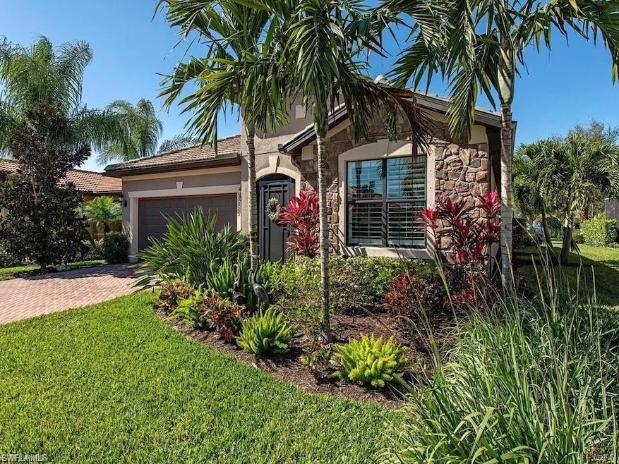 View of front of home featuring stone siding, an attached garage, stucco siding, decorative driveway, and a front lawn