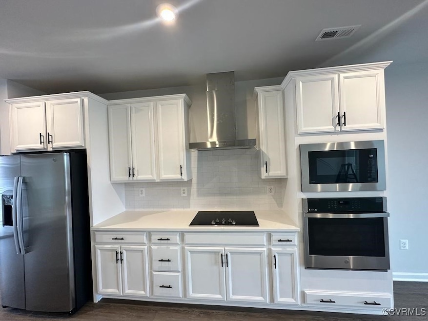 Kitchen with wall chimney range hood, stainless steel appliances, white cabinets, and dark wood-style floors