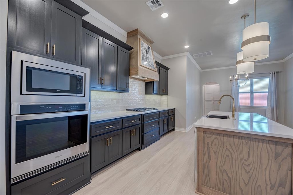Kitchen with appliances with stainless steel finishes, light countertops, light wood-type flooring, an island with sink, and crown molding