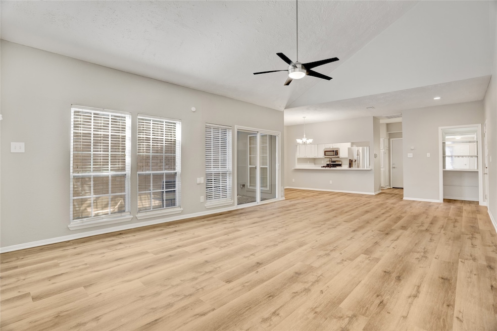 As you step inside, you’re greeted by a bright, open living space with vaulted ceilings that make the room feel even more expansive. Natural light pours in through the large windows, highlighting the clean lines and warm laminate flooring.