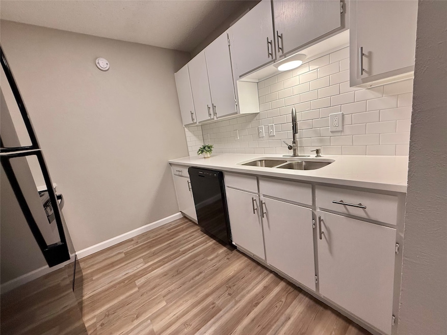 Kitchen featuring light wood-style flooring, dishwasher, white cabinets, decorative backsplash, and light stone countertops