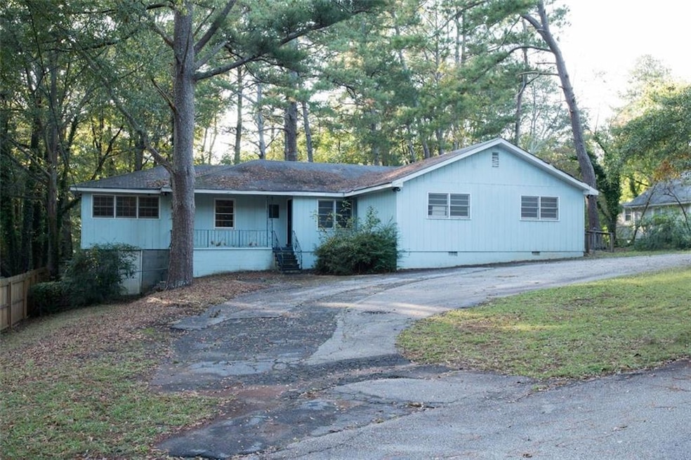 Ranch-style home with crawl space, a porch, view of wooded area, driveway, and a shingled roof