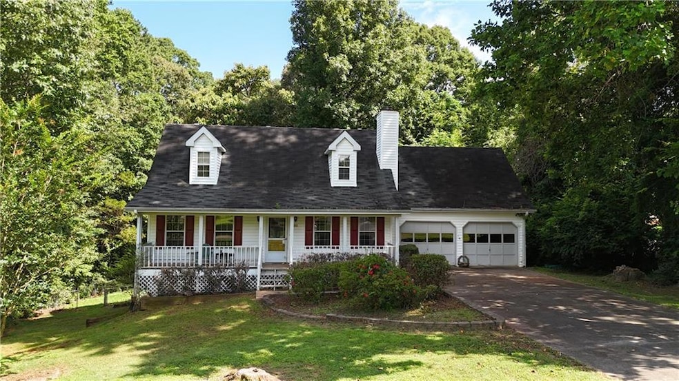 New england style home featuring a porch, a garage, concrete driveway, a chimney, and a front lawn
