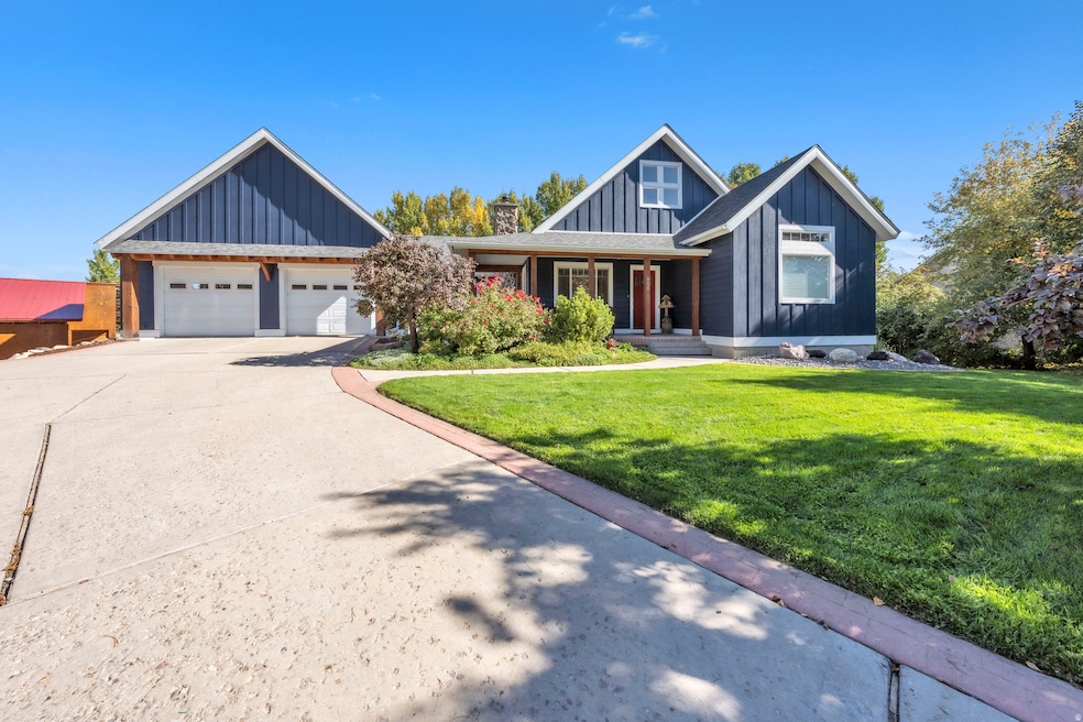 View of front of house featuring board and batten siding, covered porch, driveway, a front yard, and a garage