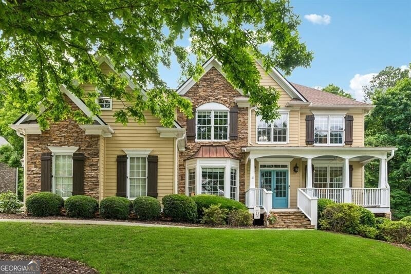 View of front facade with a front lawn, stone siding, and covered porch