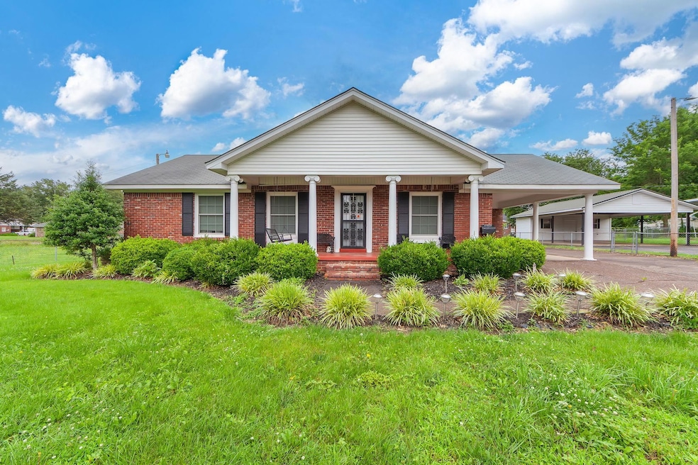 View of front of property with brick siding, a porch, a front lawn, and an attached carport