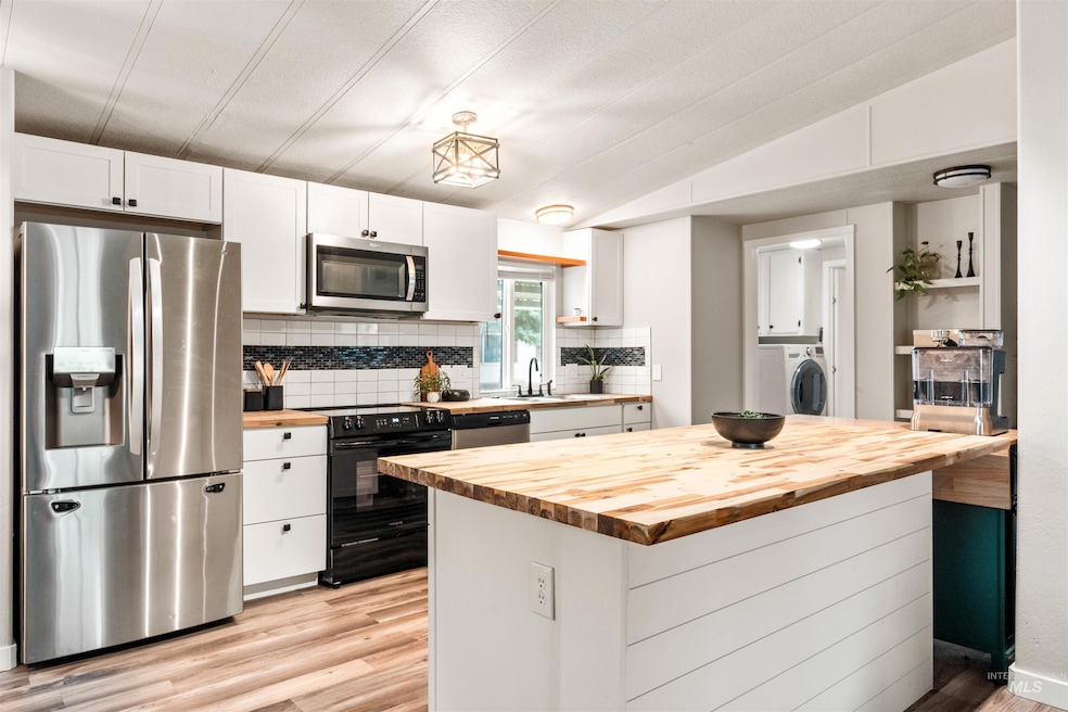 Kitchen with butcher block countertops, stainless steel appliances, backsplash, vaulted ceiling, and white cabinetry