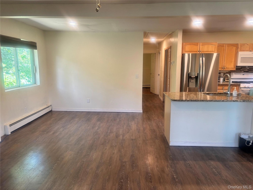 Kitchen with a baseboard heating unit, white appliances, dark wood finished floors, dark stone counters, and backsplash