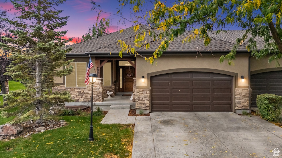 View of front of home featuring stone siding, roof with shingles, concrete driveway, an attached garage, and stucco siding