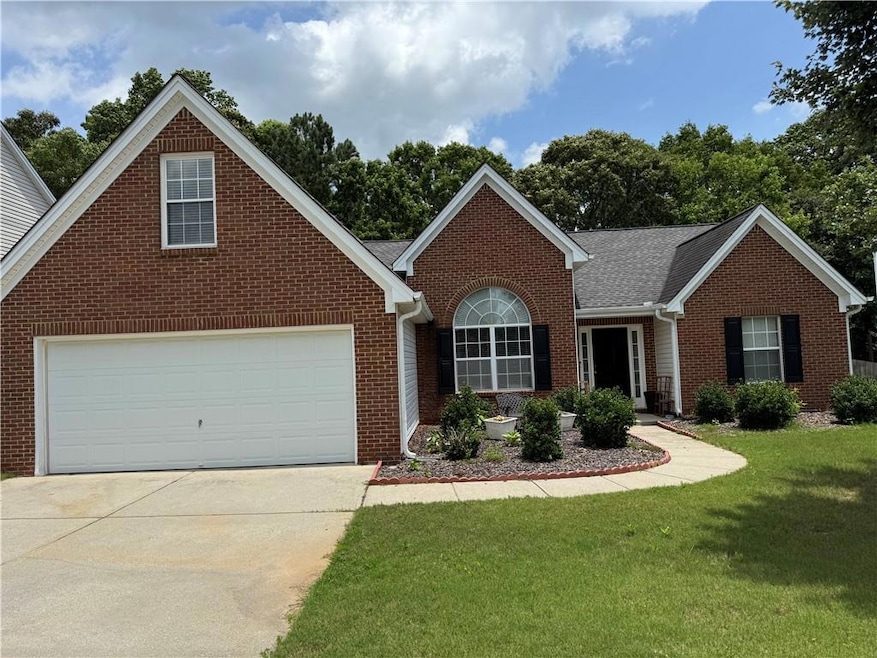 View of front facade with brick siding, a front lawn, concrete driveway, and an attached garage