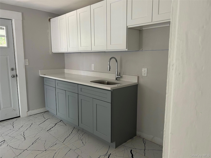 Kitchen featuring white cabinets, light marble finish floors, light stone counters, and gray cabinetry