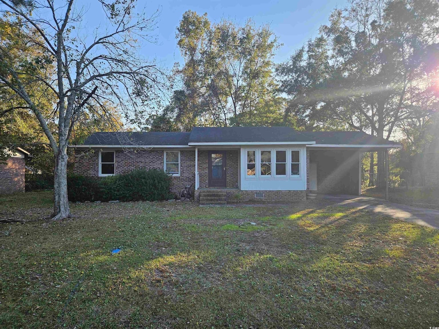 Ranch-style home featuring an attached carport, a porch, brick siding, a front lawn, and driveway